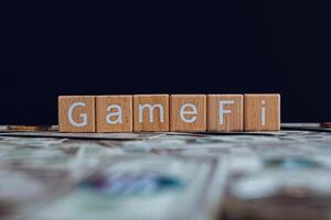 Wooden blocks with the text GameFi on a black background and crypto banknotes scattered on the ground. photo