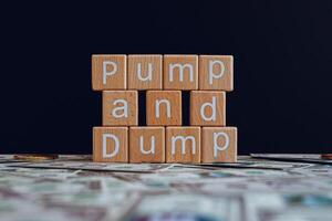 Wooden blocks with the text Pump and Dump on a black background and crypto banknotes scattered on the ground. photo