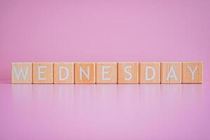 Wooden blocks form the text WEDNESDAY against a pink background. photo