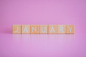 Wooden blocks form the text JANUARY against a pink background. photo