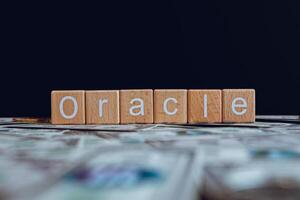 Wooden blocks with the text Oracle on a black background and crypto banknotes scattered on the ground. photo