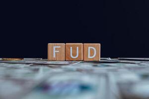 Wooden blocks with the text FUD on a black background and crypto banknotes scattered on the ground. photo