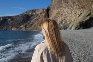 joven hermosa mujer en el costa en contra el antecedentes de rocas foto