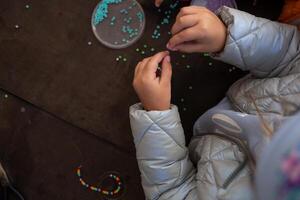 little children's hands weave a bead bracelet close-up shot photo