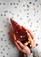 beautiful female hands holding a small red christmas tree on a gray background. photo