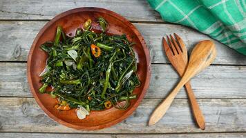 Stir fried water spinach or tumis kangkung indonesian food served on wooden plate and isolated on wooden grey table. Selective Focus. Top view. Closeup. Copy space for text photo