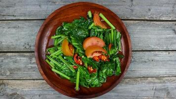 Home made food green mustard vegetables or tumis sayur sawi with sliced chilli and tomatoes on a wooden table. Grey background. photo