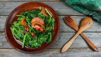 Home made food green mustard vegetables or tumis sayur sawi with sliced chilli and tomatoes on a wooden table. Grey background. photo