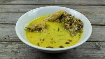 Opor Ayam is served on a wooden table. Opor is a traditional Indonesian food made from chicken cooked with coconut milk sauce photo