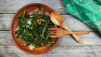 Stir fried water spinach or tumis kangkung indonesian food served on wooden plate and isolated on wooden grey table. Selective Focus. Top view. Closeup. Copy space for text photo