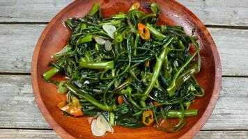 Stir fried water spinach or tumis kangkung indonesian food served on wooden plate and isolated on wooden grey table. Selective Focus. Top view. Closeup. Copy space for text photo