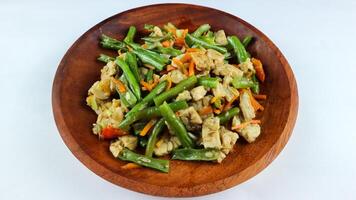 Tumis buncis, wortel and tempe or stir-fry beans, carrots and tempeh. Served on a wooden plate and isolated on a white background. photo