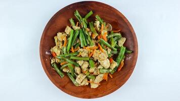 Tumis buncis, wortel and tempe or stir-fry beans, carrots and tempeh. Served on a wooden plate and isolated on a white background. photo