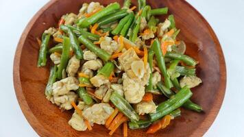 tumis buncis, wortel y tempe o Salteado frijoles, zanahorias y tempeh. servido en un de madera plato y aislado en un blanco antecedentes. foto