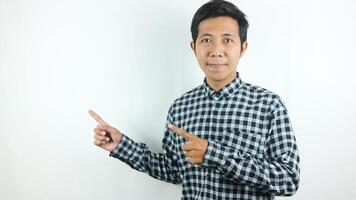 Adult Asian man wearing plaid shirt smiling while looking and pointing right side. photo