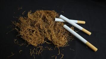 dry cut tobacco leaf, cigarettes and cigarette machine on black background. handmade cigarettes photo