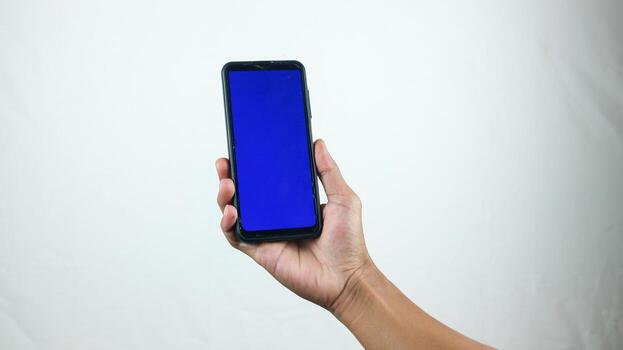 Asian man holding big smartphone with white, red, green, blue blank screen in hand, showing close to camera and pointing at device. Gadget with empty free space for mock up, banner photo