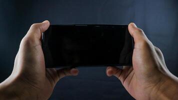 Hand holding cell phone look like playing a game blank on black screen and black background photo