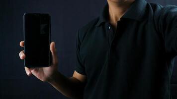 Asian man holding big smartphone with blank screen in hand, showing close to camera and pointing at device. Gadget with empty free space for mock up, banner photo