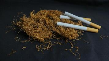 cut tobacco leaves and handmade cigarettes on black background photo
