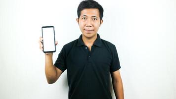 Mobile App Advertisement. Asian Man hold At Green Empty Smartphone Screen Posing Over White Studio Background, Smiling To Camera. Check This Out, Cell Phone Display Mock Up photo