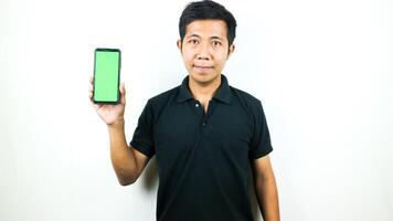 Mobile App Advertisement. Asian Man hold At Green Empty Smartphone Screen Posing Over White Studio Background, Smiling To Camera. Check This Out, Cell Phone Display Mock Up photo