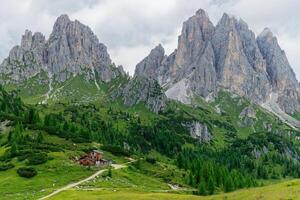 Rifugio Citta Di Carpi, Mountain Hut, with Cadini di Misurina mountains in the background in the Dolomites, Italy. Green vegetation and clouds in the sky. photo