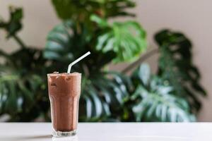 Iced cocoa in clear glass on a white table with green leaf background, Copy space for your text photo