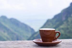 A brown coffee cup on a wooden table with a beautiful scenic view of mountains. Concept of travel and relaxation photo