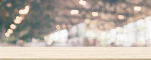 Empty wooden table top with cafe restaurant or coffee shop window interior abstract blur defocused with bokeh light background for montage product display photo