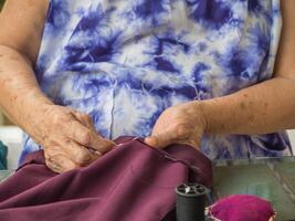Close up of older woman's hands using needle and thread to mend a pant photo