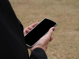 de cerca de manos mayor mujer participación un teléfono inteligente en el jardín foto