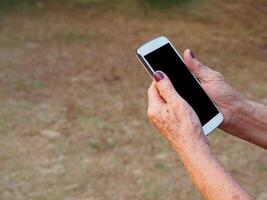 Close-up of hands senior woman holding a smartphone in the garden photo