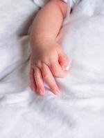 Hand of newborn showing OK gesture in sign language on white cloth. Close up of baby hand photo