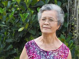 retrato de un mayor mujer sonriente y mirando a cámara mientras en pie en un jardín foto