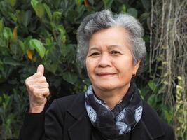 A senior Asian woman with short white hair smiling and looking at the camera while standing in a garden photo