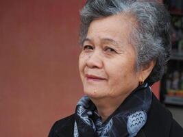 An elderly Asian woman looking at the camera with a warming friendly smile while sitting in the garden photo