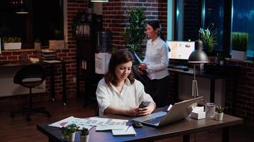 souriant directeur à la recherche à texte messages sur téléphone intelligent, prise Pause de travail sur entreprise projet. équipe chef dérouler par en utilisant téléphone à Feuilleter social médias dans bureau, caméra une video