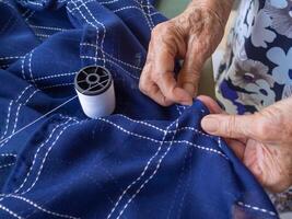 Close-up partial view of old woman hands using needle and thread to mend cloth. photo