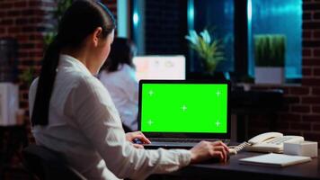 Worker looking over green screen laptop display, researching key data for company project. Businesswoman analyzing figures and charts on chroma key electronic device in office at night video