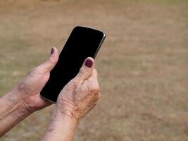 Close-up of hands senior woman holding a smartphone in the garden photo