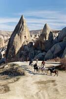 People riding horses on the Rose Red Valley in Cappadocia, Turkey. Famous destination for people to explore the Rock Sites of Cappadocia. photo