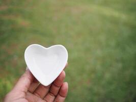 Hand of woman holding a white ceramic heart on blur green background photo