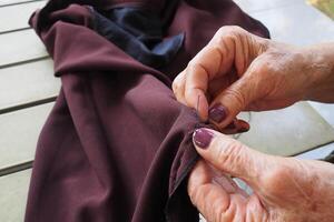 Close-up of hands old woman sewing cloth while sitting in balcony photo