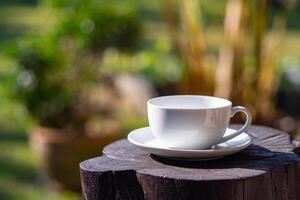 A white cup of coffee on wooden table with nature background in the garden photo