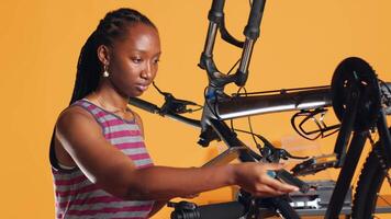 Engineer with tablet in hand analyzing damaged bike over studio background awaiting repair and maintenance. Woman using electronic device to diagnose bicycle on repair stand, camera A video