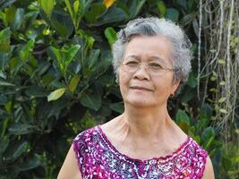 Senior woman with short white hair smiling and looking at camera while standing in a garden photo