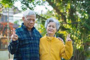 Portrait of romantic elderly man with his wife and showing victory gesture with fingers in the garden photo