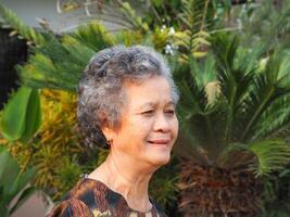 Side view of a senior woman smiling and looking away while standing in a garden photo
