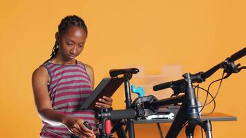 femme Suivant l'Internet Didacticiel clips sur tablette, apprentissage à réparer sa endommagé vélo. cyclisme amateur Suivant guider sur Comment à faire entretien pour vélo Composants, studio arrière-plan, caméra une video